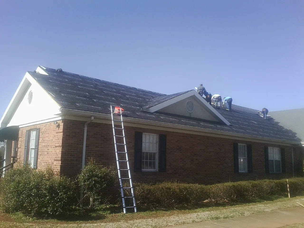 Crew tearing shingles off a brick ranch roof with a ladder set — Metal Roof Repair work by our crew in Fairfax