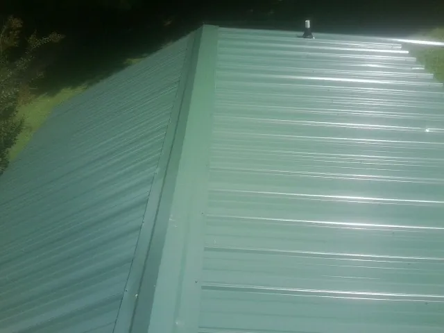 New green metal panels meeting at the ridge of a roof — Flat Roof Repair work by our crew in Fairfax